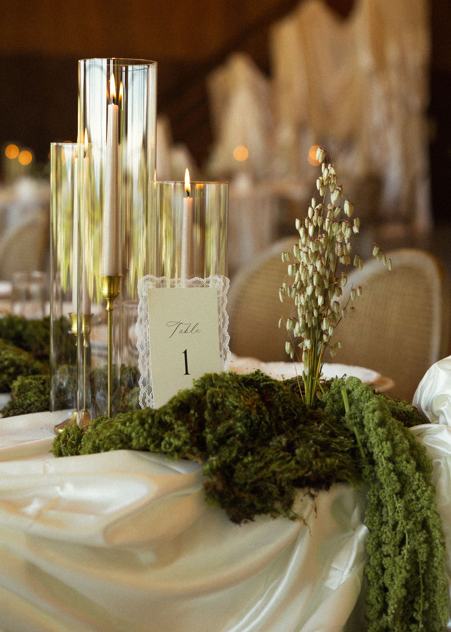 Taper candles in glass hurricanes beside a lace table number